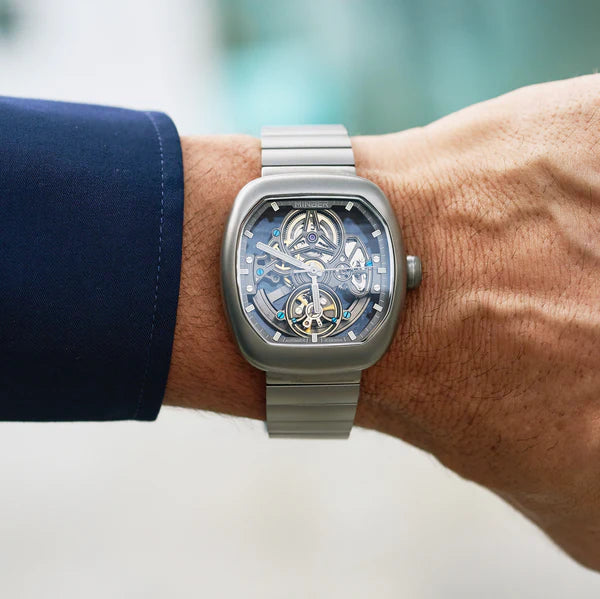 Luxury skeleton watch with bold square case, inspired by motorsport design, worn on wrist with blue sleeve.