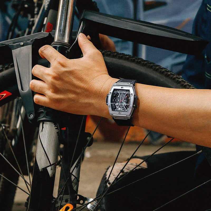 Sport-luxury square chronograph watch with skeleton dial on wrist, shown gripping a bicycle.