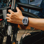 Sport-luxury square chronograph watch with skeleton dial on wrist, shown gripping a bicycle.
