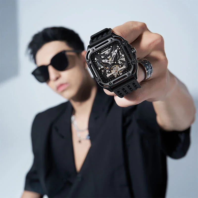 Man wearing black sunglasses showcasing a modern square skeleton sport-luxury watch with a black band