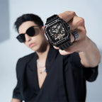 Man wearing black sunglasses showcasing a modern square skeleton sport-luxury watch with a black band